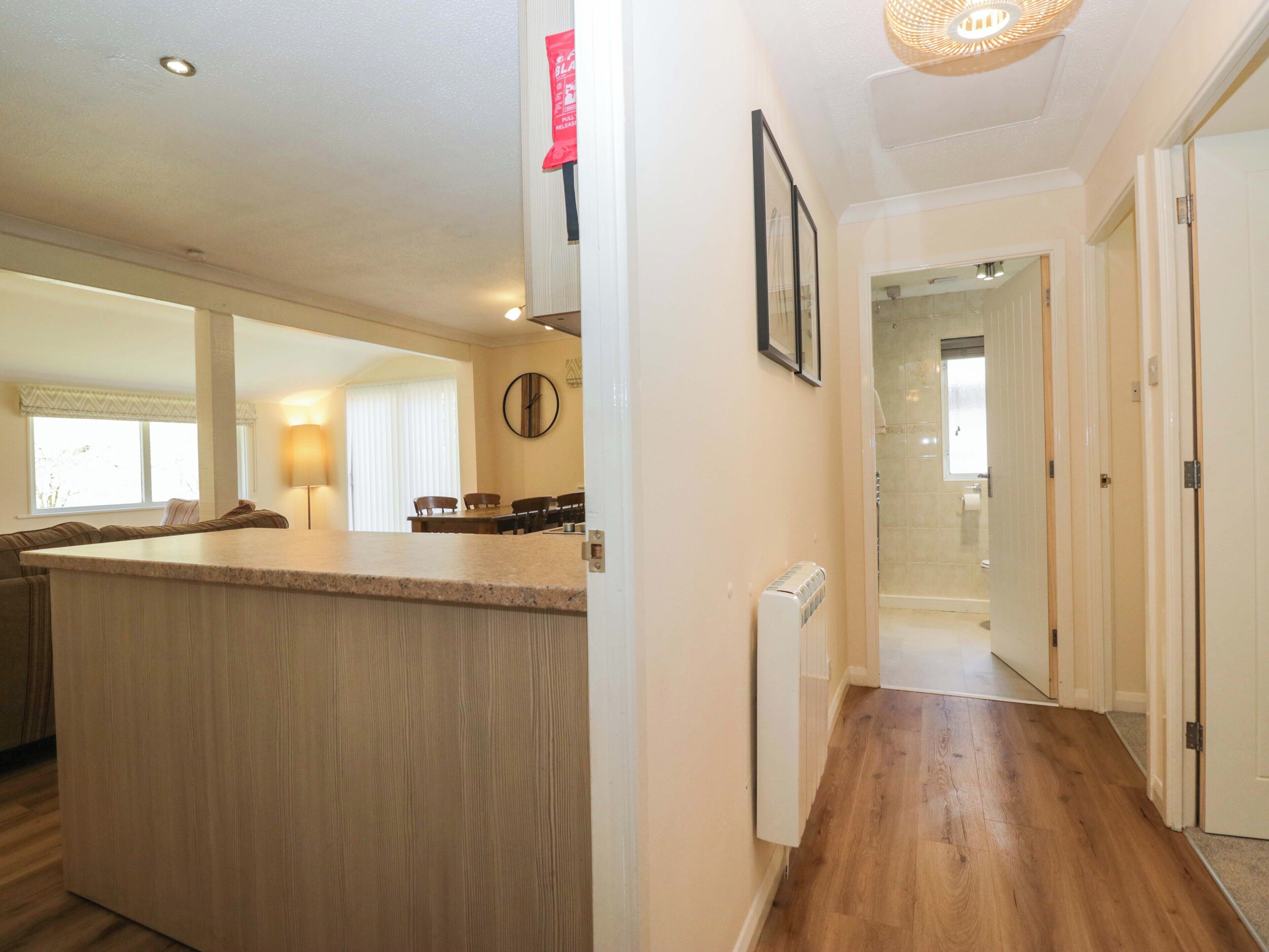 A modern kitchen with a central island, a dining area with chairs, a hallway leading to a bathroom, and a door on the right.