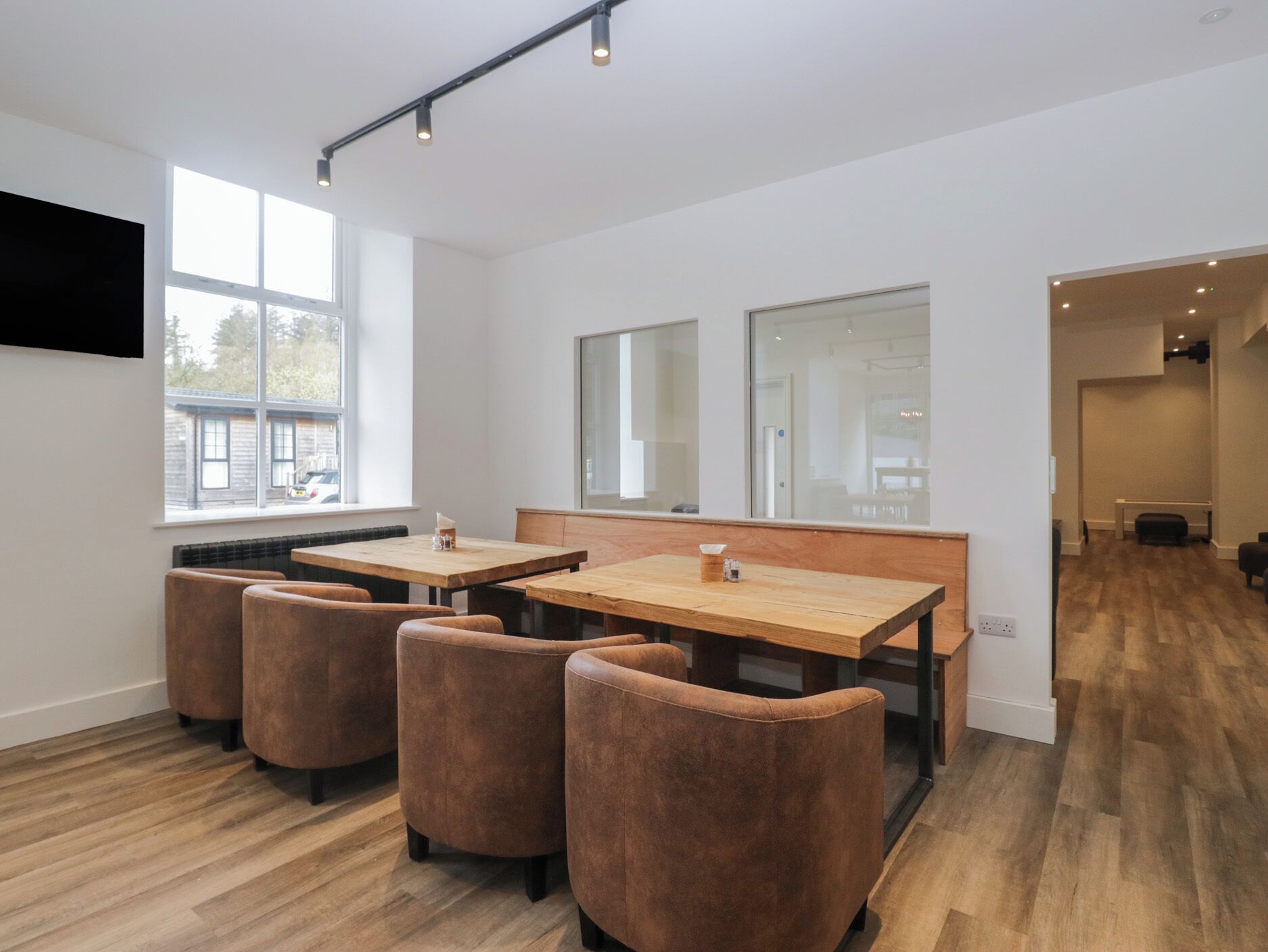 A modern interior with a wooden table and chairs, large windows, and a flat-screen TV mounted on the wall.