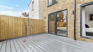 A modern building with a wooden deck, a glass door leading to a bedroom, and a brick exterior. - Modern 3 Bedroom Stay, Patio, East Croydon (Greater London)