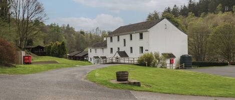 A white building with a sloped roof, a paved driveway, and a grassy area with a wooden fence.