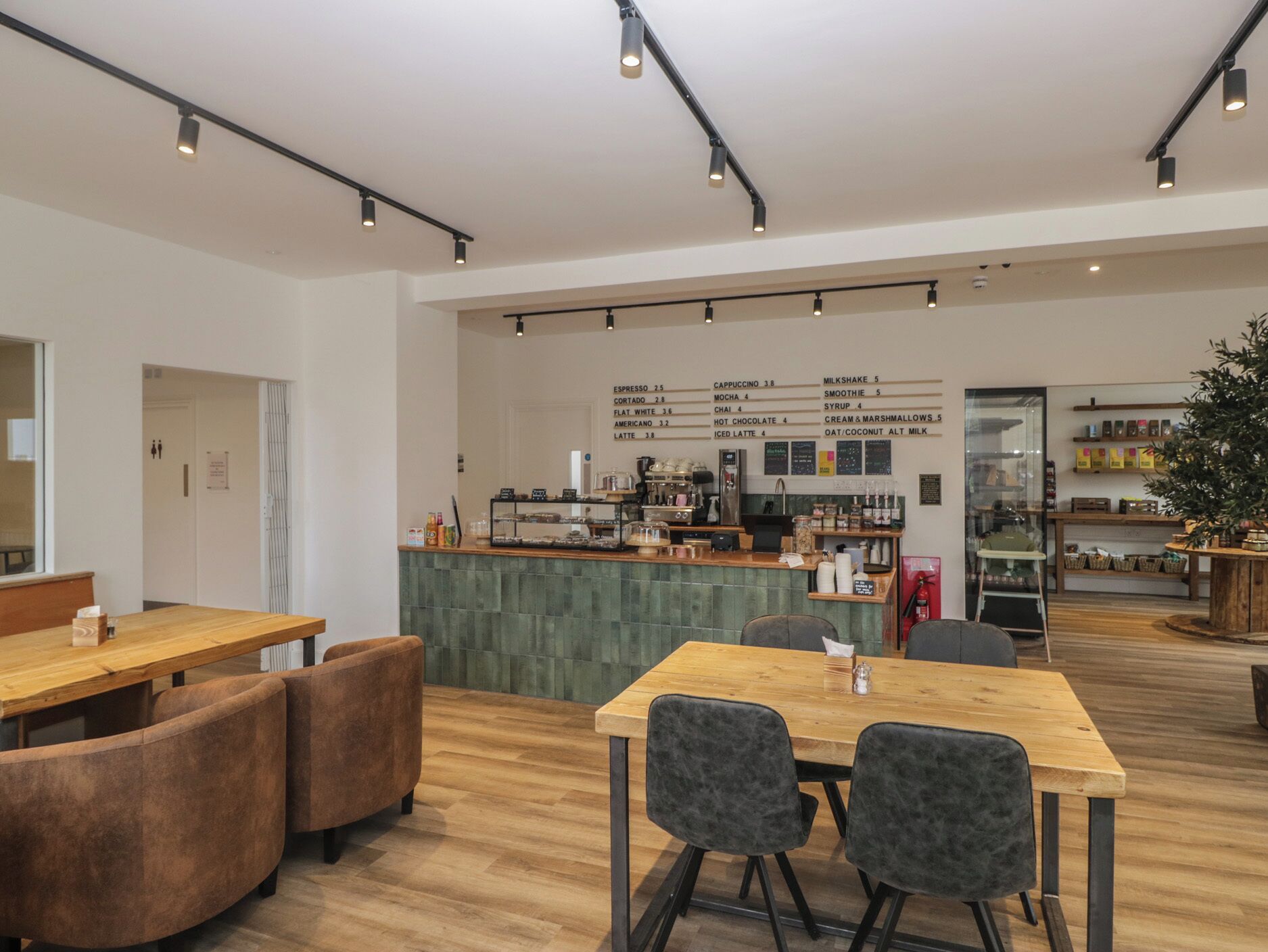 Un café moderno con mesas y sillas de madera, una barra con diferentes opciones de café, y un menú a la vista.