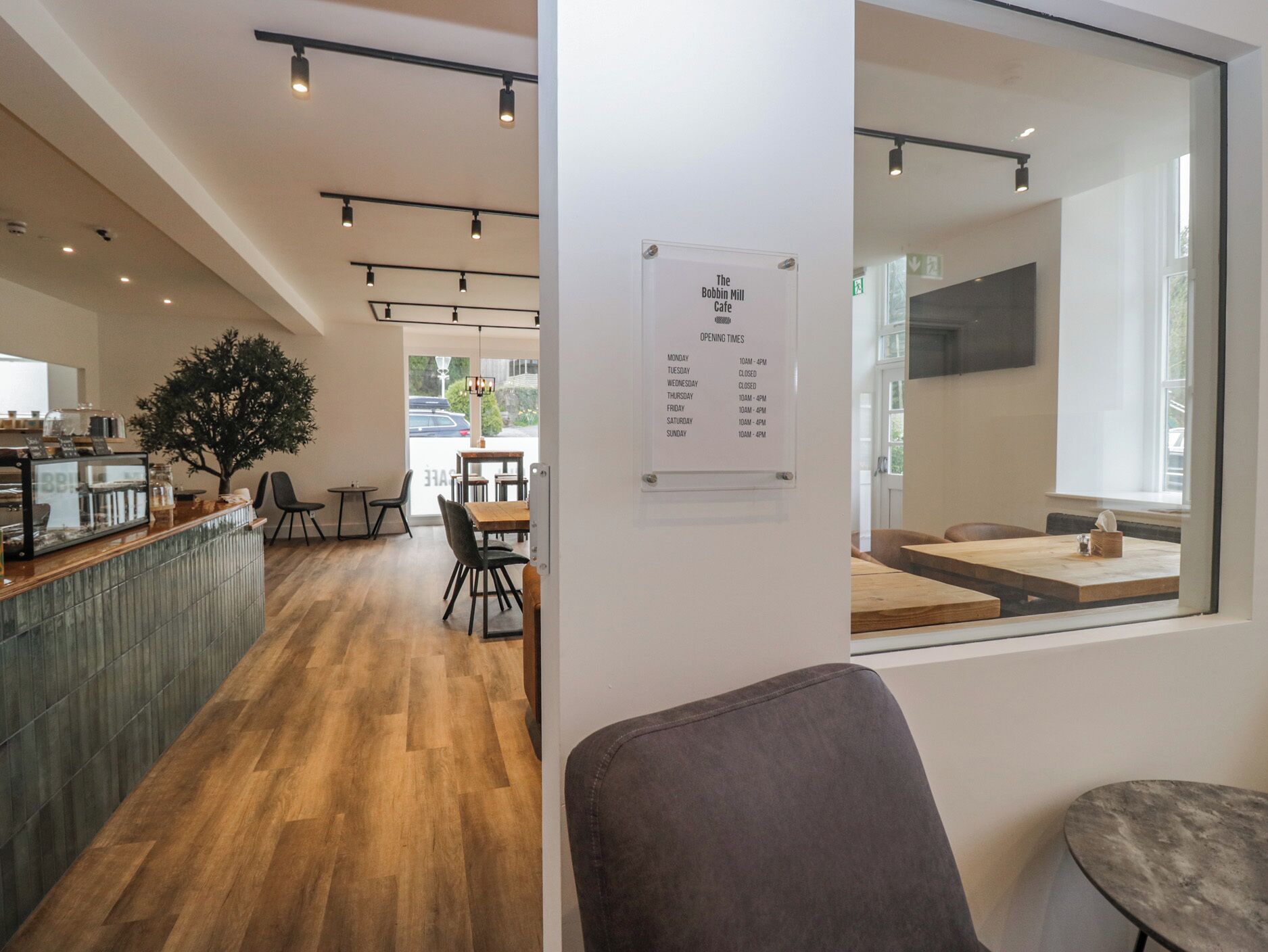 A cafe interior with wooden flooring, a reception desk, and a seating area with tables and chairs.