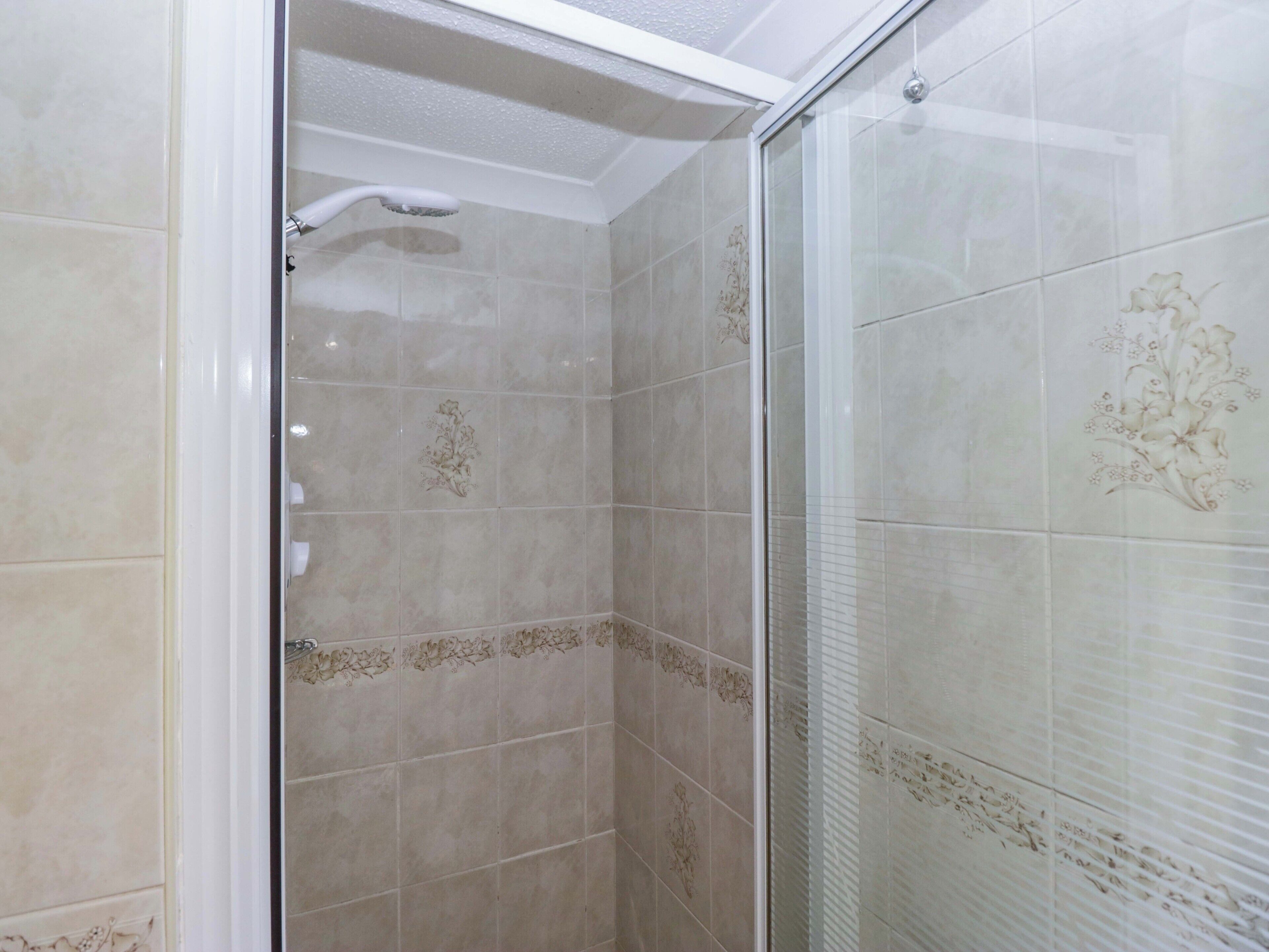 Una ducha con puerta de vidrio, baldosas beige con diseños florales y techo blanco.