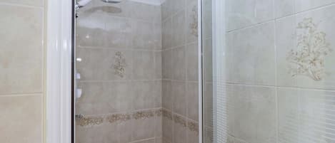 Una ducha con puerta de vidrio, baldosas beige con diseños florales y techo blanco.