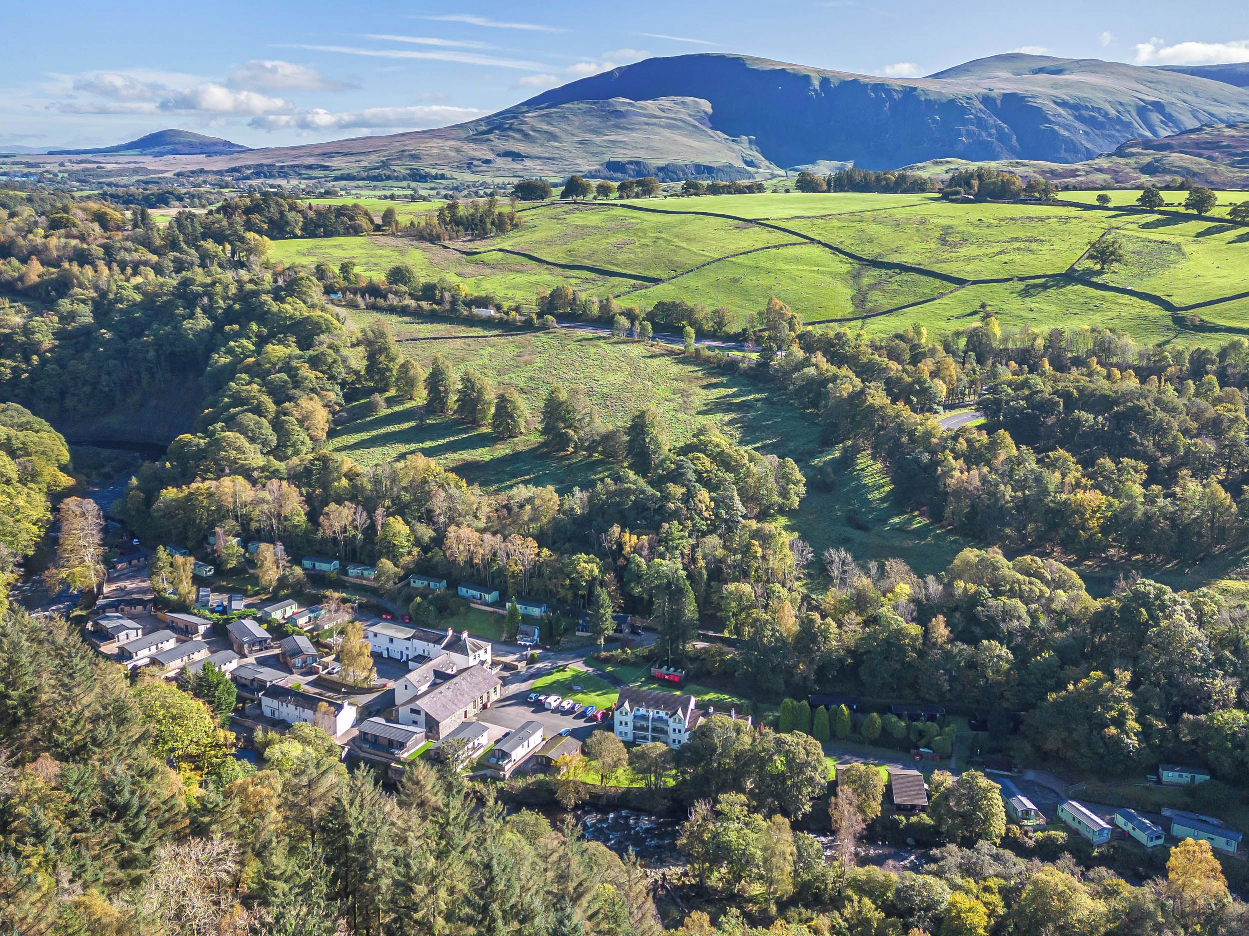 A rural village with houses, a road, and rolling hills in the background.