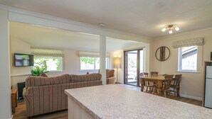 A modern kitchen with a granite countertop, a dining area with wooden chairs, a sofa, and a television. - Chestnut Timber Lodge (Keswick)