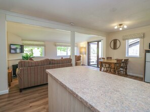 A modern kitchen with a granite countertop, a dining area with wooden chairs, a sofa, and a television. - Chestnut Timber Lodge (Keswick)