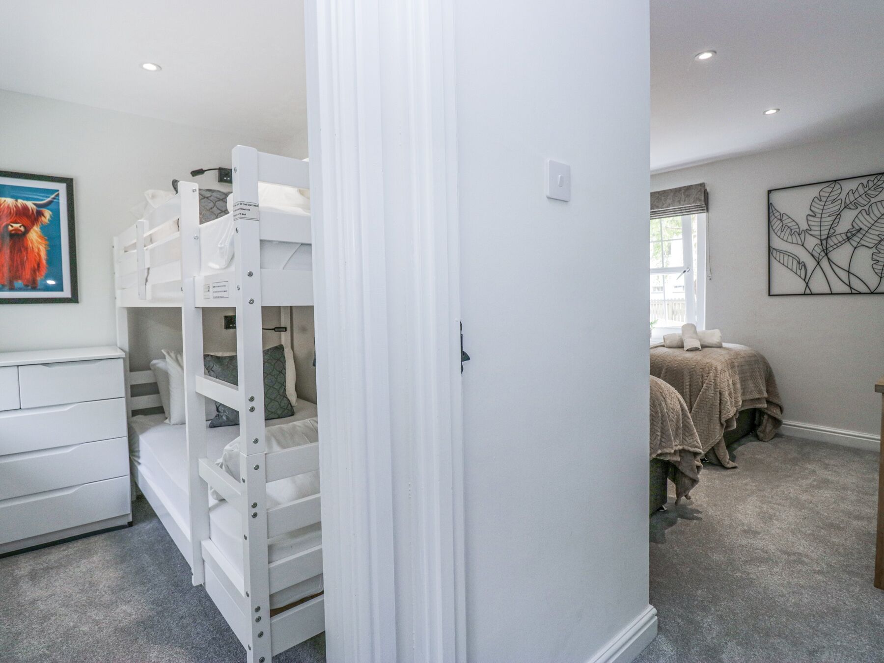 A room with bunk beds, a white dresser, a framed picture, and a window with curtains.