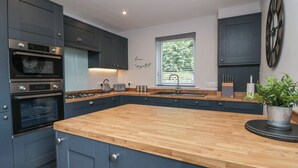 Een moderne keuken met donkere kastjes, een houten aanrechtblad, ingebouwde apparatuur en een raam met jaloezieën.