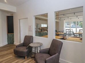 Ein modernes Interieur mit zwei Sesseln, einem kleinen runden Tisch und einem großen Fenster, das einen Cafébereich reflektiert.