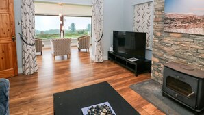 A living room with a TV, a fireplace, and a view of the outdoors. - Casey House (Castletownbere)