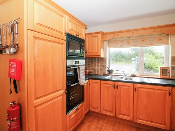 Una cocina con armarios de madera, un horno negro, un microondas y una ventana con vistas a la vegetación.