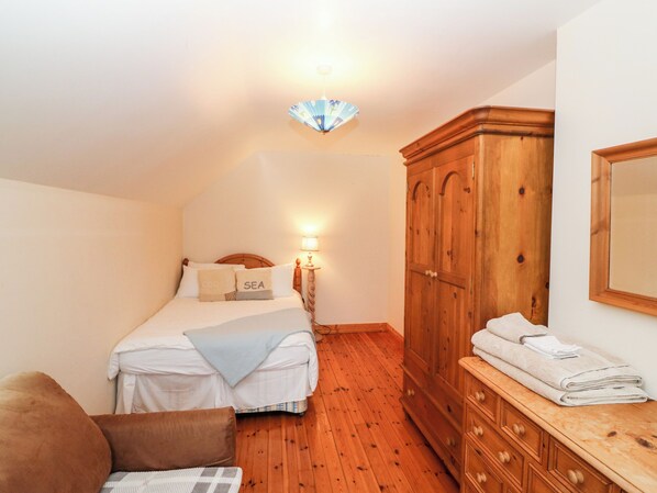 A bedroom with a bed, a wooden wardrobe, a bedside table with towels, and a wall-mounted lamp. - Casey House (Castletownbere)