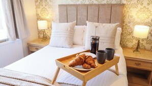 Egy szállodai szoba, amelyben egy ágy, két éjjeliszekrény, egy tálca, rajta croissant-okkal, egy kávéfőző és két csésze található.