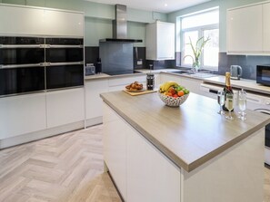 A modern kitchen with built-in ovens, a central island with fruit and drinks, and a large window providing natural light. - Chalfont Lodge (Skegness)