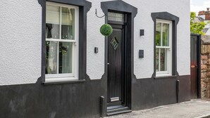A two-story house with a black front door, white windows, and a small garden. - The Old Sweet Shop (Conwy)