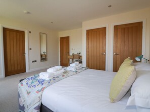 A hotel room with a large bed, two wooden doors, a desk with a chair, and a mirror on the wall. - Lower Mellan Barn (Helston)