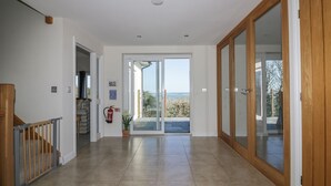 A spacious hallway with a wooden staircase, a fire extinguisher, and a view through the glass doors to the outside.