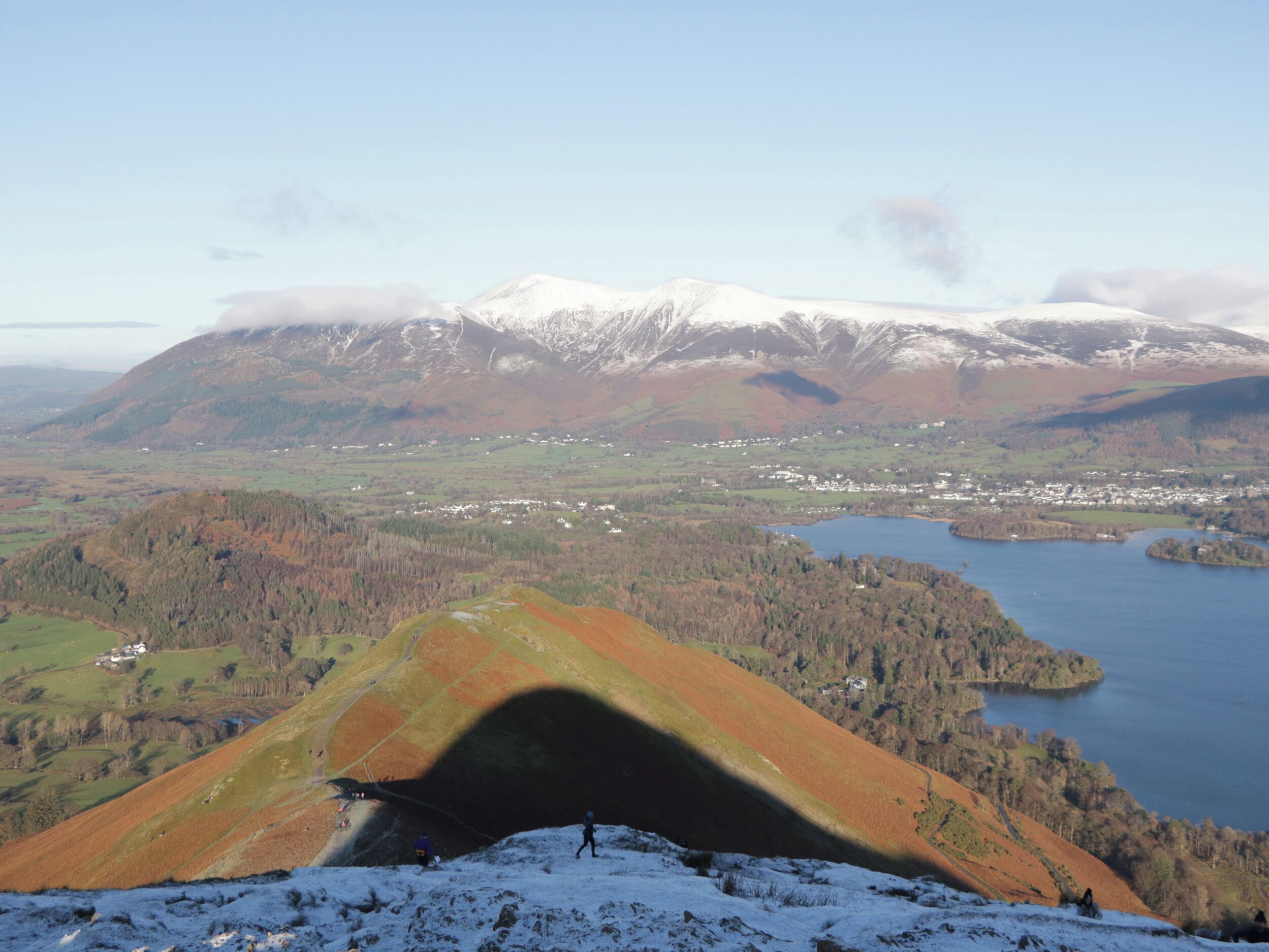 Vista panor âmica de uma paisagem montanhosa com um lago, um pequeno povoado e picos nevados ao longe.