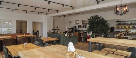 A modern cafe with wooden tables, a menu board, and a bar area.