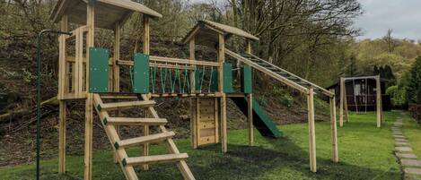 A wooden playground structure with a slide, climbing net, and a small shelter.