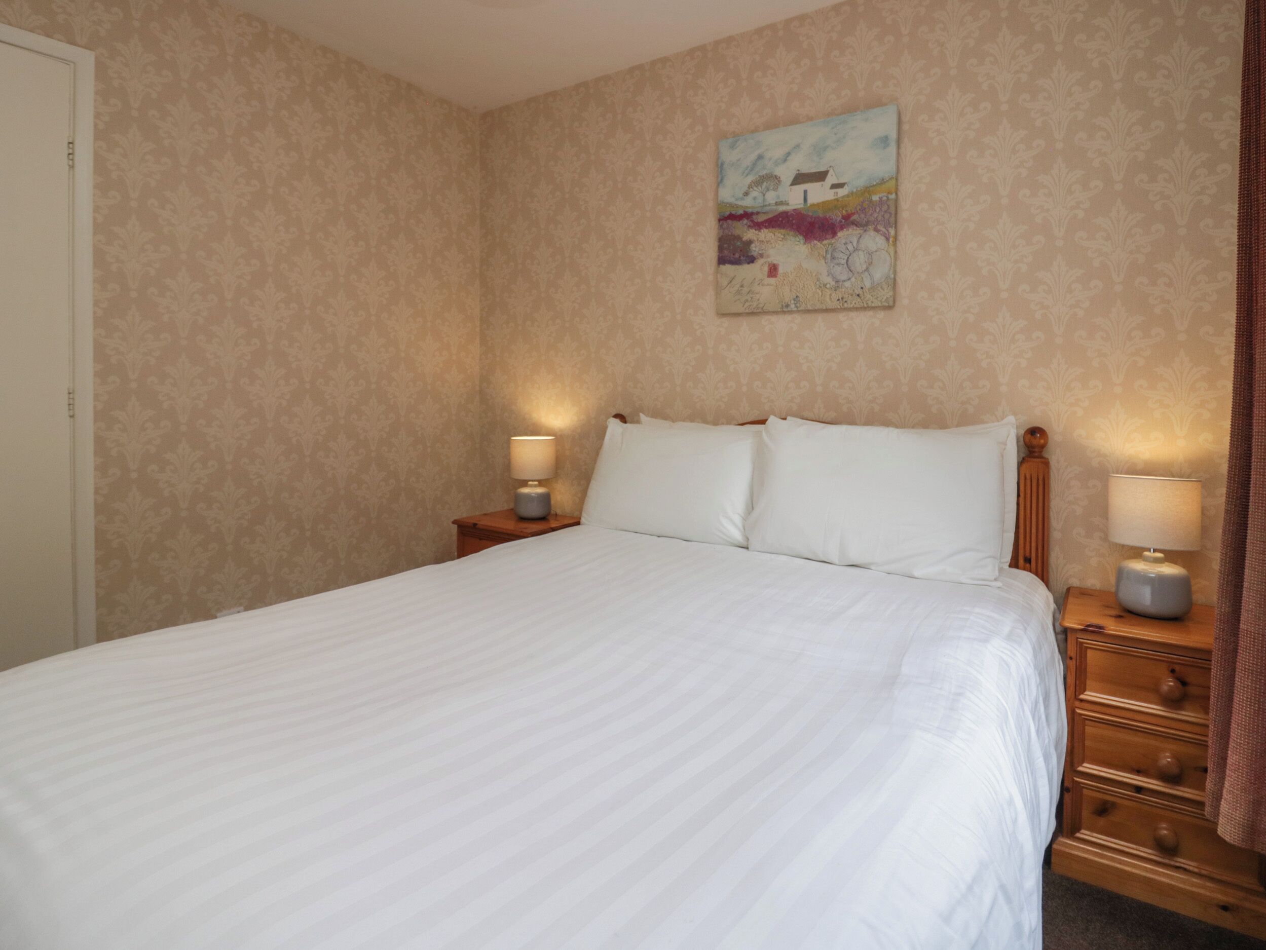 A neatly made bed with white linens, two bedside tables with lamps, and a painting on the wall.
