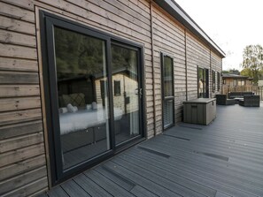 A wooden cabin with large sliding glass doors, a deck with outdoor furniture, and a small attached structure with a window. - The Bothy (Keswick)