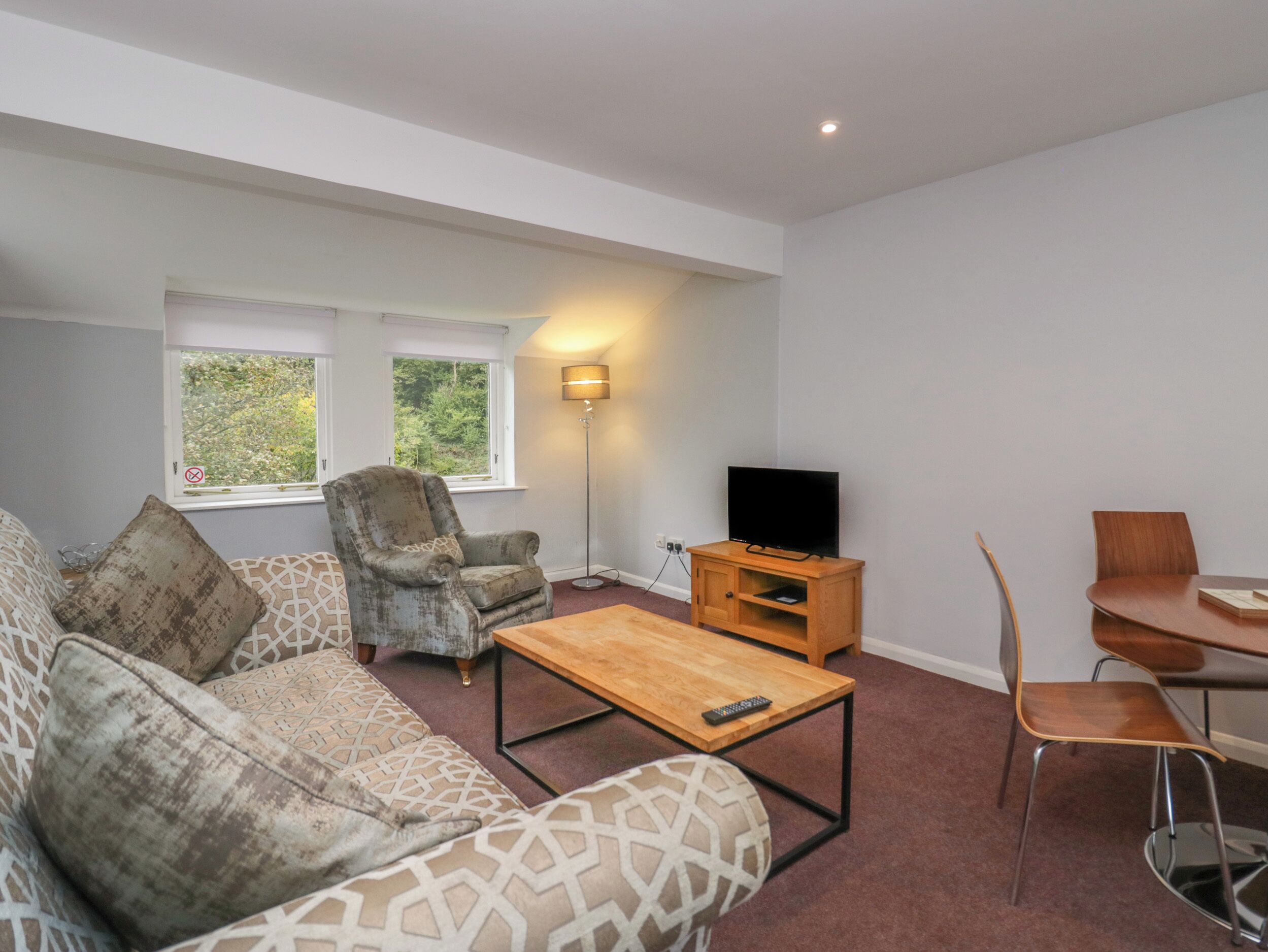 Una sala moderna con sofá, sillón, mesa de centro, mueble para televisión y comedor.