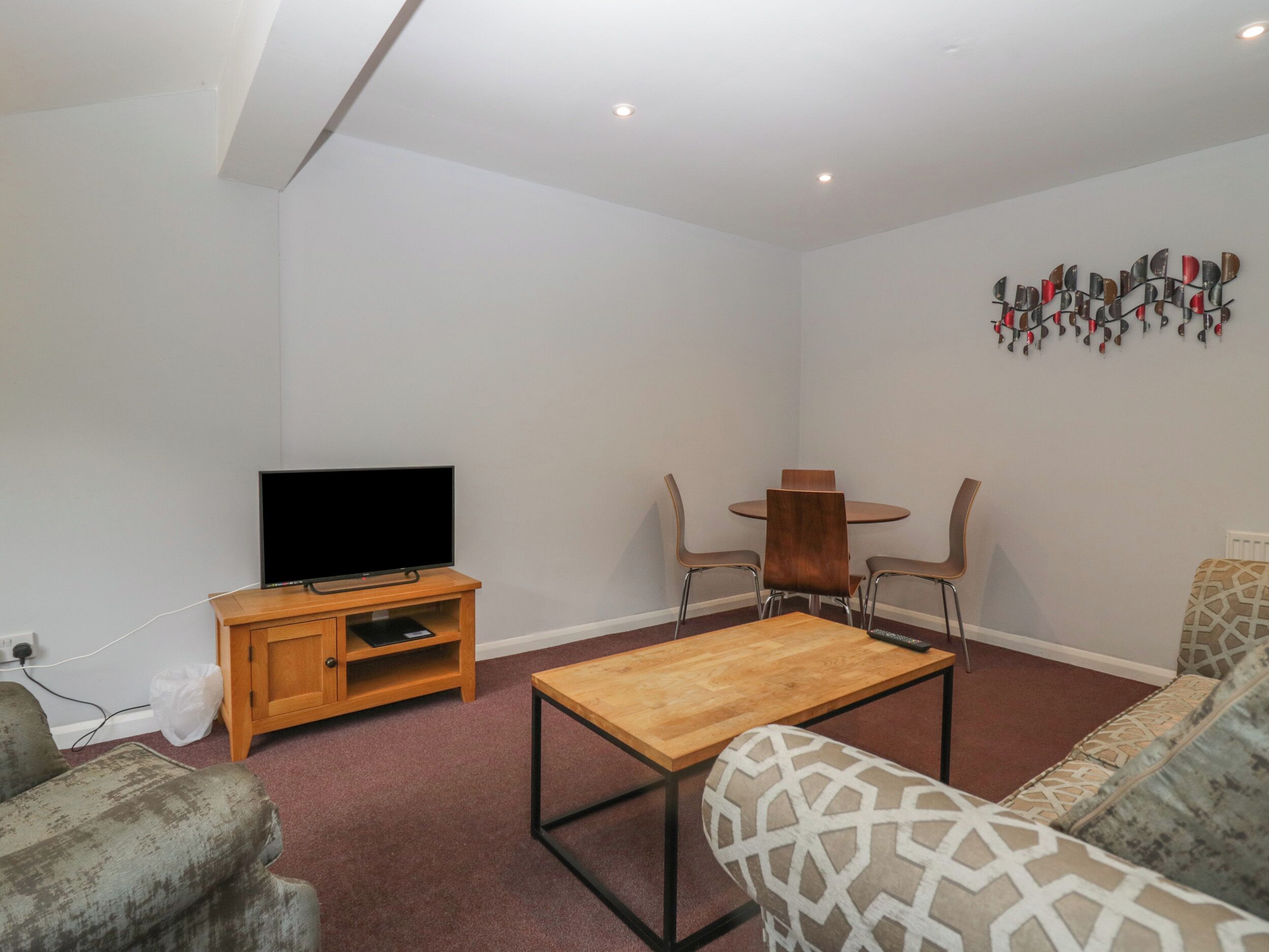 A living room with a TV on a wooden stand, a coffee table, two chairs, and a sofa.