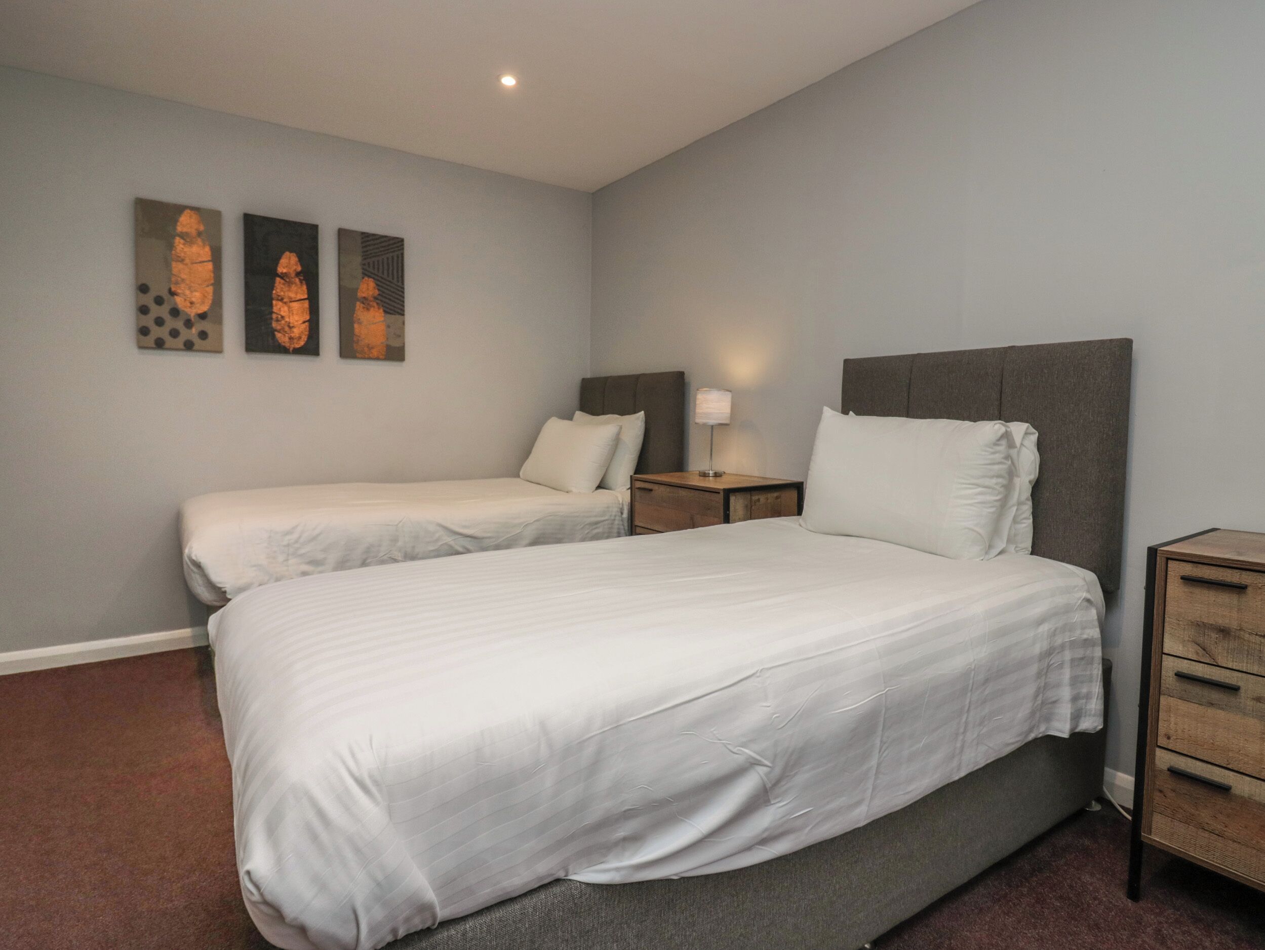 Une chambre avec deux lits simples, une table de chevet avec une lampe et une commode.