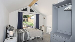 Une chambre à coucher comprenant un lit, une table de chevet, une lampe, une commode et une vue sur l’extérieur.