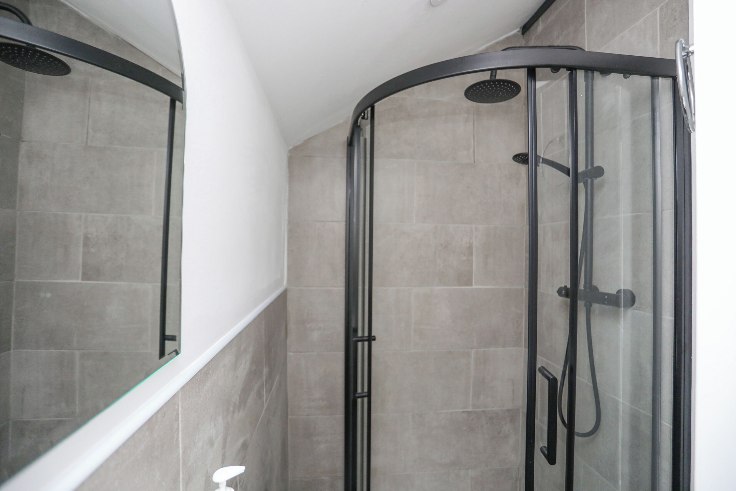 A glass-enclosed shower with a curved design, tiled walls, and a white ceiling.