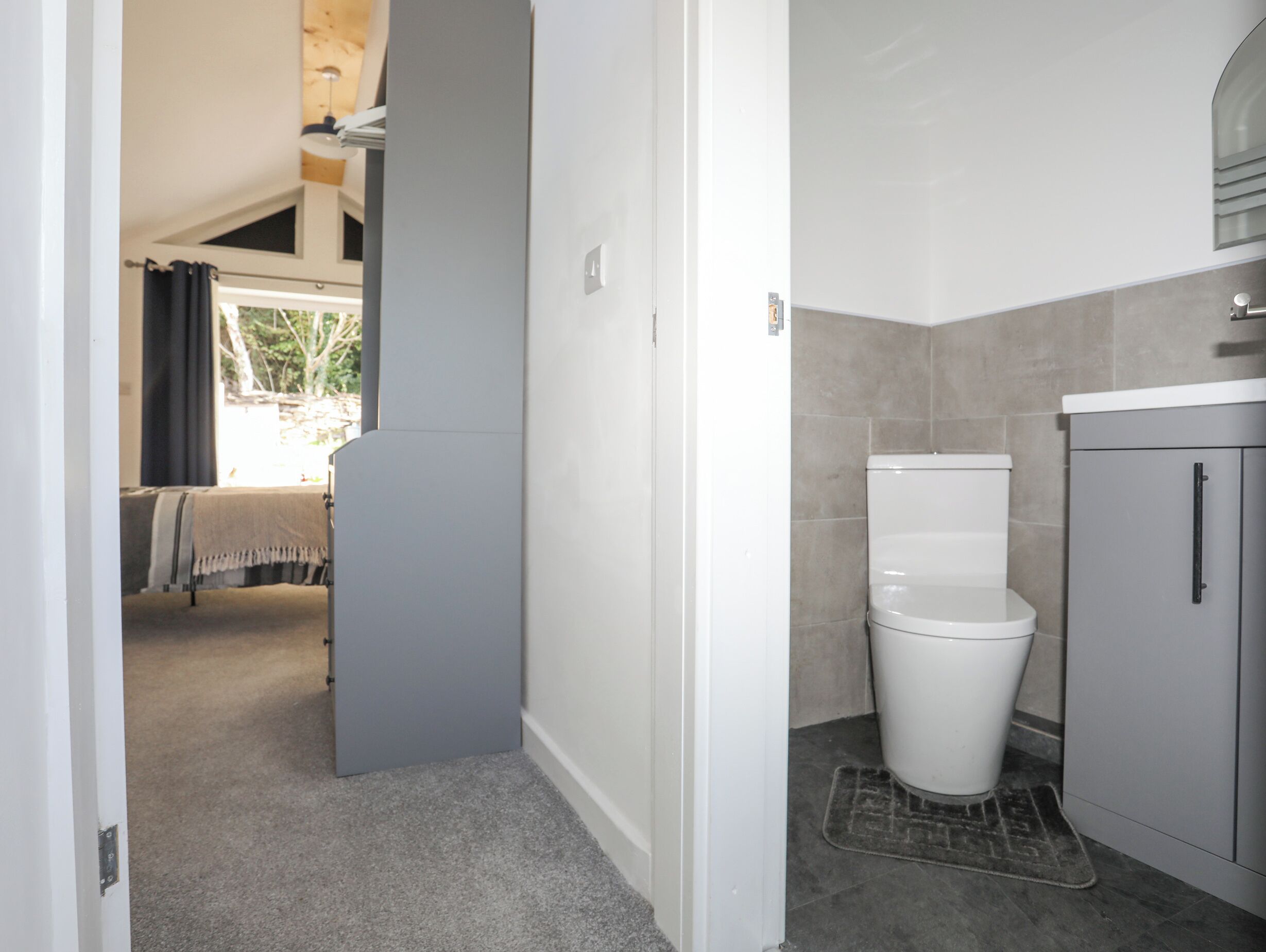 Une salle de bain avec des toilettes, un lavabo et un meuble de rangement. Une porte donne accès à une autre pièce.