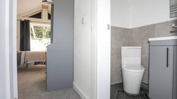 Une salle de bain avec des toilettes, un lavabo et un meuble de rangement. Une porte donne accès à une autre pièce.