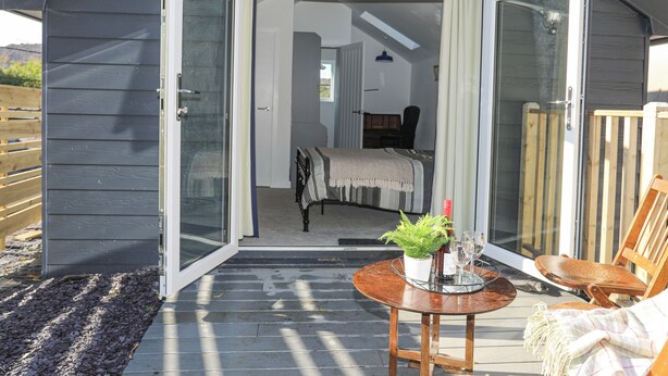 Une cabane confortable avec une porte-fenêtre coulissante donnant sur une chambre à coucher équipée d’un lit et d’un fauteuil.