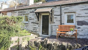 Une maison en pierre avec un banc en bois à l’extérieur, une porte et une fenêtre.