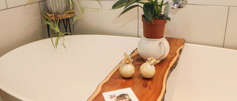 A bathroom with a wooden tray holding toiletries and a photograph, surrounded by potted plants.