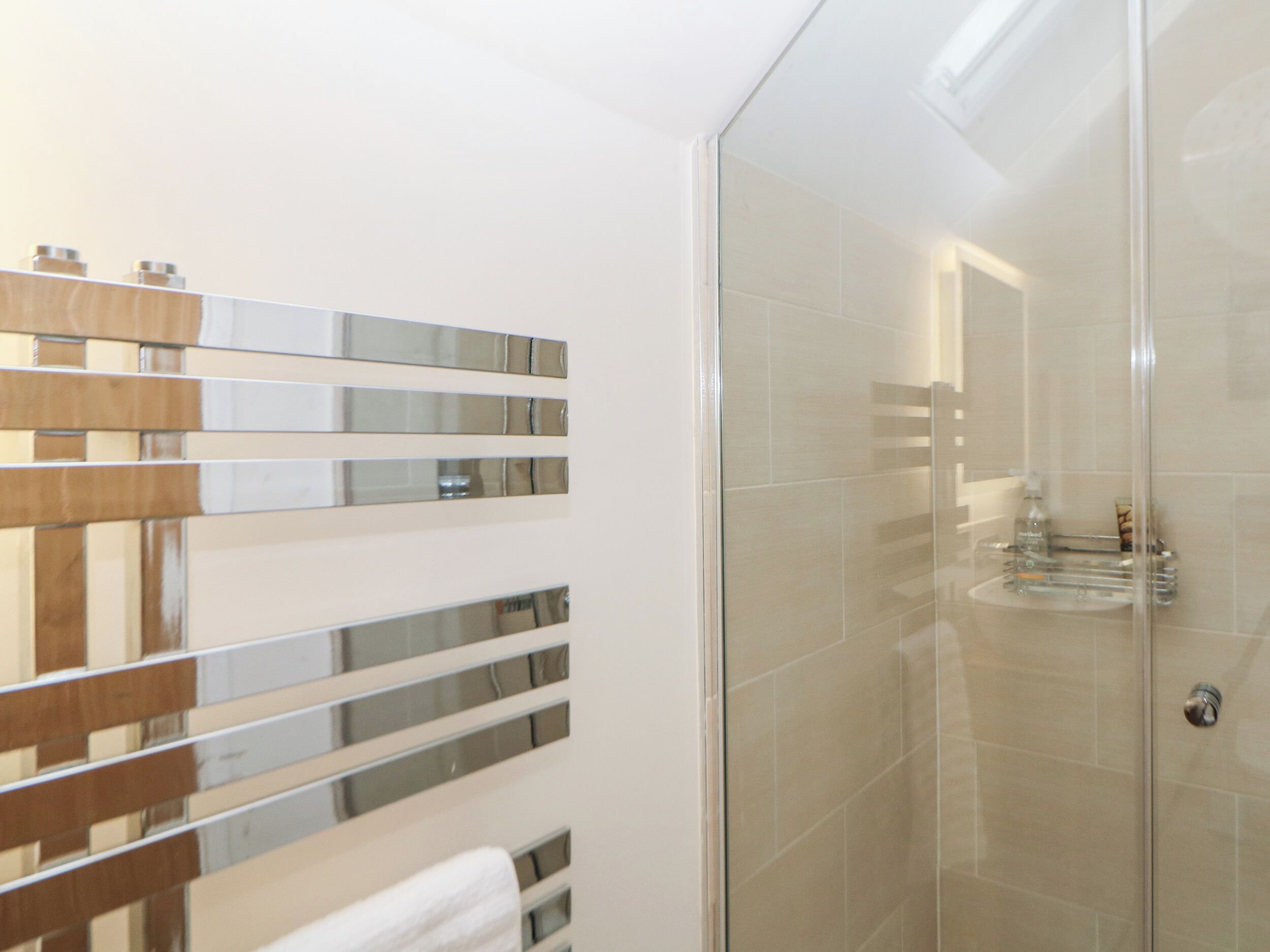 A modern bathroom with a glass shower enclosure, a wooden towel rack, and a mirrored wall.