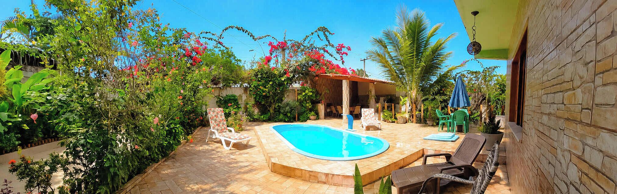 A swimming pool with lounge chairs and a covered seating area surrounded by lush greenery.