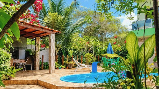 Un'area piscina con un solarium in legno, una zona salotto coperta e rigogliosa vegetazione.