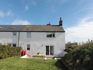 A two-story house with a sloped roof, a chimney, and a small front yard with a bench and potted plant. - Little Haven (Bamburgh)