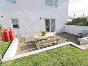 A white building with a wooden table and benches, a potted plant, and red gas cylinders in the yard. - Little Haven (Bamburgh)