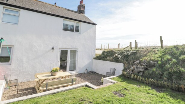 A white house with a patio, a wooden table, and a bench. - Little Haven (Bamburgh)