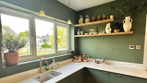 A kitchen with dark green walls, a white countertop, and a window with a view of the outside. - The Shingles (Sandown)