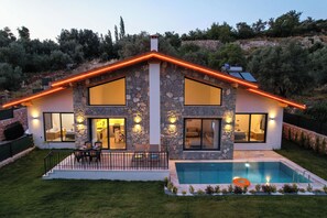 A modern house with a stone facade, large windows, a swimming pool, and outdoor seating.
