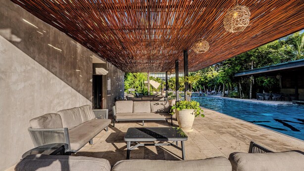 A covered outdoor seating area with a pool, lounge chairs, and a potted plant.