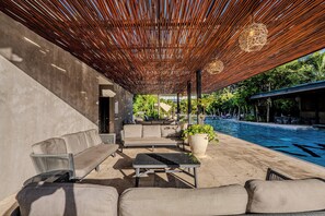 A covered outdoor seating area with a pool, lounge chairs, and a potted plant.