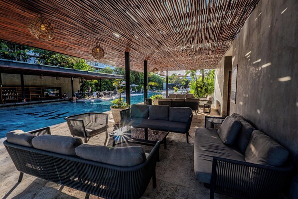 An outdoor lounge area with a pool, wicker furniture, and a modern ceiling design.