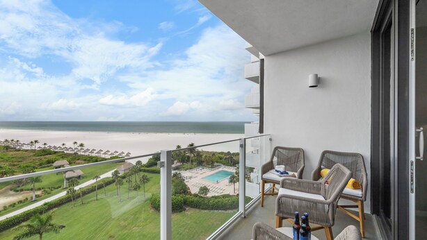 A balcony with wicker furniture, a pool, and a view of the beach and ocean. - SW Facing Beachfront Condo | Sweeping Ocean Views (Marco Island)