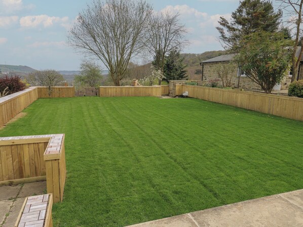 Un patio trasero bien cuidado con una terraza de madera, un muro de piedra y vistas del paisaje circundante.